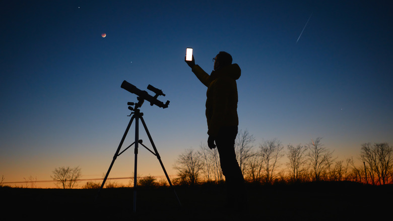 Silhouette d'un homme debout à côté d'un télescope prenant des photos du ciel nocturne 