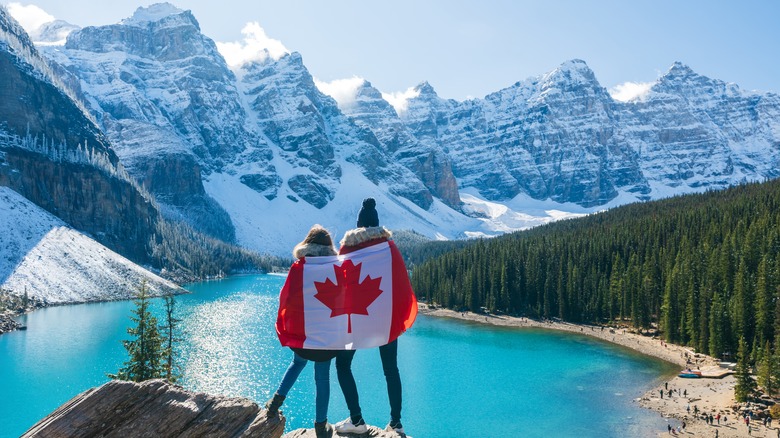 Couple de voyageurs drapés dans le drapeau canadien devant le lac Moraine